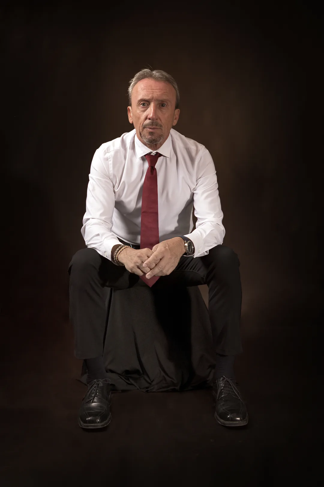 Paco Gumiel sentado, con camisa blanca y corbata granate, sobre fondo oscuro